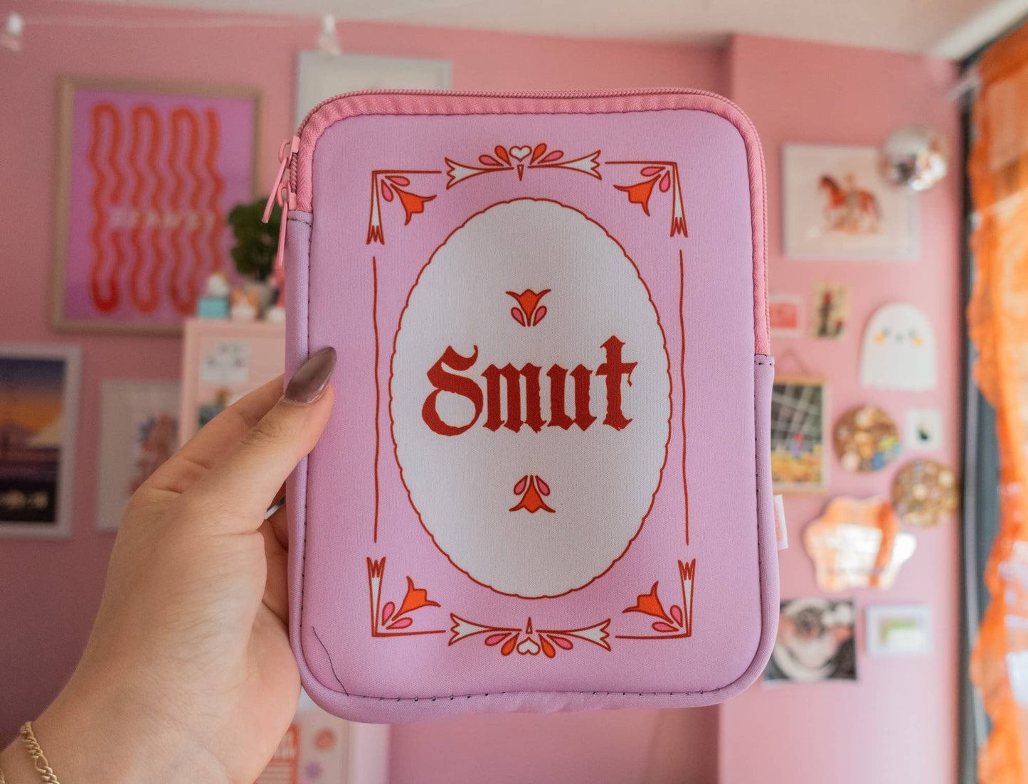 Pink case with 'Smut' text held in front of a pink wall with posters.
