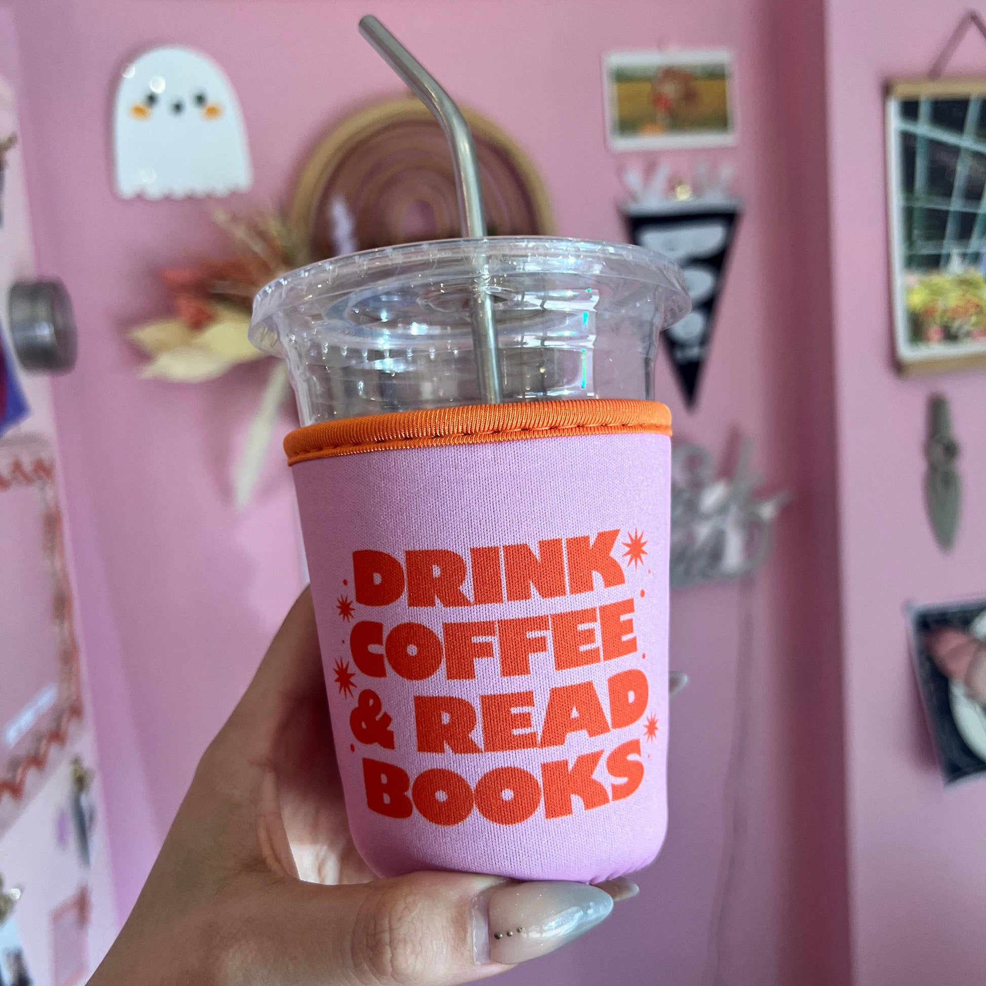 Pink tumbler with 'Drink Coffee & Read Books' text held in front of a pink wall.