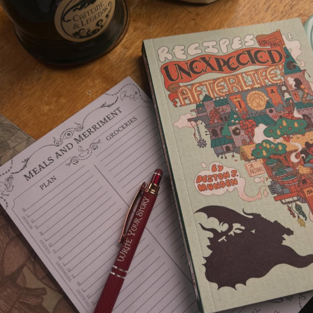 Notebook, pen, and mug on a wooden surface with a book titled 'Recipes Unexpected' visible.