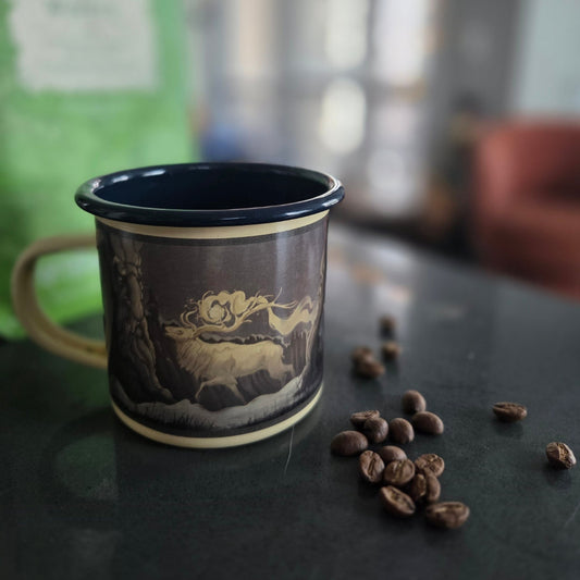 Decorative mug with a gold design on a dark surface with coffee beans.